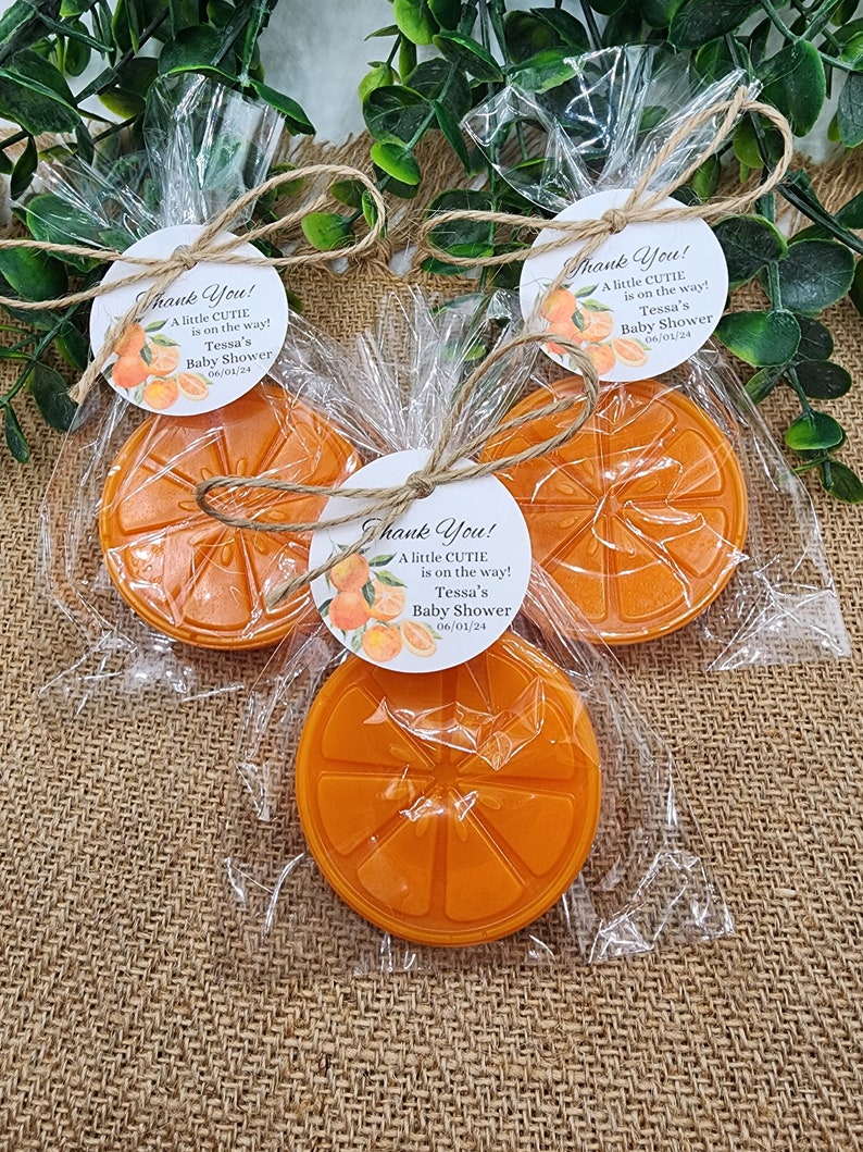 May include: Three orange-scented soap favors wrapped in cellophane bags with twine and a round tag that says "Thank You! A little cutie is on the way! Tessa's Baby Shower 06/01/24"