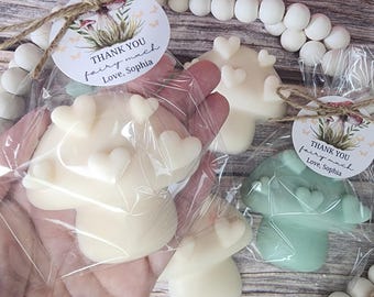 May include: Mushroom-shaped soaps in ivory and mint green, decorated with heart accents, are packaged in clear cellophane. Each soap is tied with twine and a circular tag that reads "Thank you fairy much Love, Sophia."