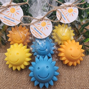 May include: Four small yellow and blue sun-shaped soaps with smiley faces, packaged in clear cellophane bags with a small round tag that reads "Here comes the Son! Thank you for brightening our day!"