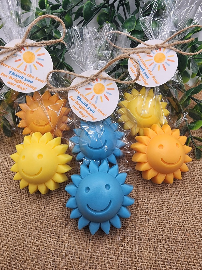 May include: Four small yellow and blue sun-shaped soaps with smiley faces, packaged in clear cellophane bags with a small round tag that reads "Here comes the Son! Thank you for brightening our day!"
