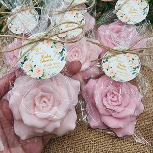 May include: Pink rose-shaped soap favors wrapped in clear cellophane bags with a brown twine bow and a round floral tag that reads "Keishla & Donald's Baby Shower Thank You! 06.08.2024".