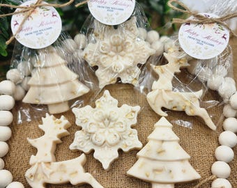 May include: Holiday-themed soaps in the shapes of snowflakes, reindeer, and Christmas trees. Each soap is individually wrapped in clear cellophane and tied with twine. The soaps have a light beige color with gold accents. Each package has a circular tag that reads "Happy Holidays FROM THE WILLIAMS 2025".
