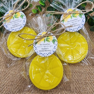 May include: Three clear cellophane bags with yellow lemon-shaped soap bars and a round white tag with blue and green floral designs. The tag says "She found her main squeeze Sophia's Bridal Shower".