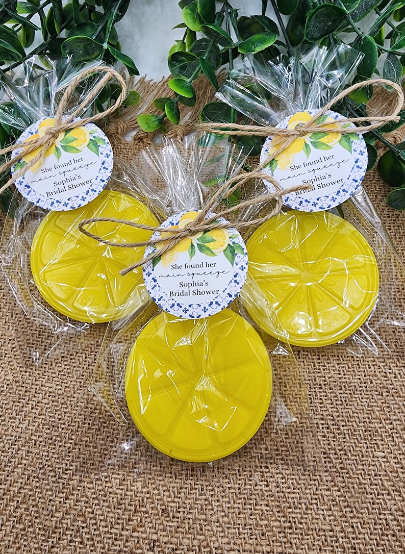 May include: Three clear cellophane bags with yellow lemon-shaped soap bars and a round white tag with blue and green floral designs. The tag says "She found her main squeeze Sophia's Bridal Shower".