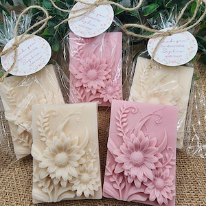 Puede incluir: Cuatro peque&ntilde;as barras rectangulares de jab&oacute;n con dise&ntilde;os florales. Dos barras son rosas con flores blancas y dos barras son blancas con flores rosas. Cada barra est&aacute; envuelta en celof&aacute;n transparente y atada con una cuerda. Una peque&ntilde;a etiqueta redonda con el texto "&iexcl;Gracias por duchar a Sophia con amor!" est&aacute; unida a cada barra.