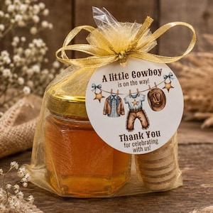 May include: A small glass jar filled with golden honey, enclosed in a sheer gold organza drawstring bag with a wooden honey dipper. A round white tag attached to the gold ribbon features the text A little Cowboy is on the way! Thank You.