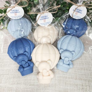 May include: Blue and white favor boxes with a teddy bear hot air balloon design. The boxes are tied with twine and have a small tag that says "Ashley's Baby Shower" and "Thank you for showering our baby with love".