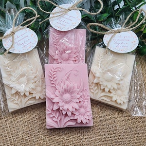 Puede incluir: Tres peque&ntilde;as bolsas de regalo con envoltura de celof&aacute;n transparente, cada una contiene una pastilla de jab&oacute;n con dise&ntilde;o floral. Las pastillas de jab&oacute;n son blancas y rosas con un dise&ntilde;o floral en relieve. Las bolsas est&aacute;n atadas con cuerda y tienen peque&ntilde;as etiquetas redondas con el texto "&iexcl;Gracias por celebrar a Sophia con amor!"