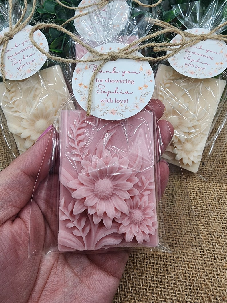 Puede incluir: Pastilla de jab&oacute;n floral rosa envuelta en celof&aacute;n con una etiqueta redonda de agradecimiento que dice "&iexcl;Gracias por celebrar a Sophia con amor!"