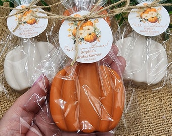 May include: Fall in Love! Sophia's Bridal Shower 10.14.23. A small orange pumpkin-shaped soap is wrapped in clear cellophane with a white tag tied with twine. The tag has a floral design with a pumpkin and the text "Fall in Love! Sophia's Bridal Shower 10.14.23".