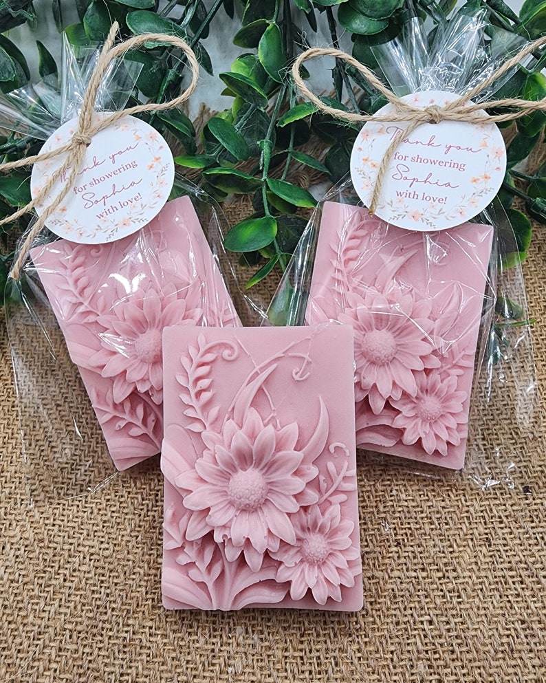 Puede incluir: Tres favores de jab&oacute;n floral rosa envueltos en bolsas de celof&aacute;n transparentes atadas con cuerda y una peque&ntilde;a etiqueta redonda que dice "&iexcl;Gracias por celebrar a Sophia con amor!"