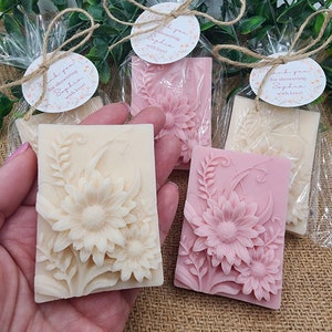 Puede incluir: Cuatro peque&ntilde;as barras rectangulares de jab&oacute;n con dise&ntilde;os florales. El jab&oacute;n est&aacute; envuelto en celof&aacute;n transparente y atado con cuerda. Cada jab&oacute;n tiene una peque&ntilde;a etiqueta redonda adjunta con el texto "&iexcl;Gracias por celebrar a Sophia con amor!"