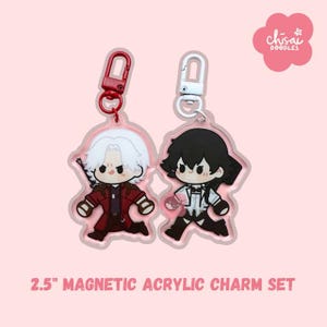 May include: Two acrylic charm keyrings featuring cartoon characters, each with a different hairstyle and outfit. The charms are 6.35 cm in size and have red and white metal clasps. The text "2.5" MAGNETIC ACRYLIC CHARM SET" is printed at the bottom.