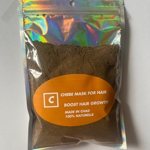 May include: A resealable silver pouch filled with a brown powder. The pouch has a label with the text "Chebe Mask for Hair Boost Hair Growth Made in Chad 100% Naturelle" and a letter "C" in a square.