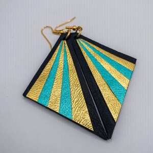 May include: A pair of black leather earrings with gold and turquoise geometric patterns. The earrings are shaped like triangles with rounded corners.