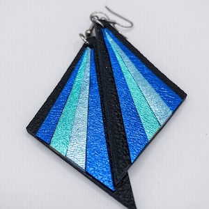 May include: A pair of blue and black leather earrings with a geometric design. The earrings are shaped like a diamond and have a silver hook.