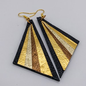 May include: A pair of black leather earrings with gold and brown stripes. The earrings are shaped like triangles with rounded corners.