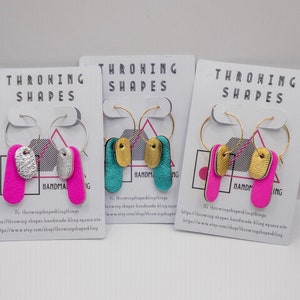 May include: Three pairs of handmade earrings with gold hoops and two different coloured leather shapes. The earrings are displayed on white cards with the text "THROWING SHAPES" and the website address "https://www.etsy.com/shop/throwingshapesbling".
