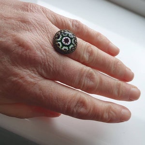 Puede incluir: Un anillo con un diseño de mosaico redondo, blanco, verde y rojo engastado en un engaste de latón.