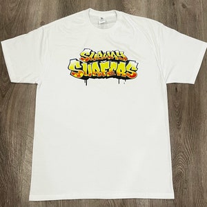May include: White t-shirt featuring the Subway Surfers logo in a graffiti-style design. The logo is in yellow, orange, and red with black dripping accents. The shirt is made of a soft, comfortable material.