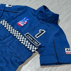 May include: Blue racing jumpsuit with a checkered stripe, a peace sign with an American flag design, and the text "Liam A RH#" and the number "1".