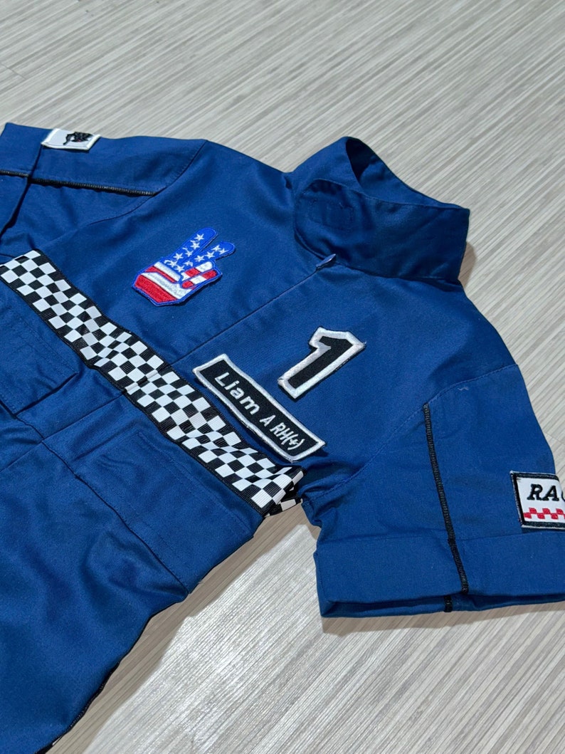 May include: Blue racing jumpsuit with a checkered stripe, a peace sign with an American flag design, and the text "Liam A RH#" and the number "1".