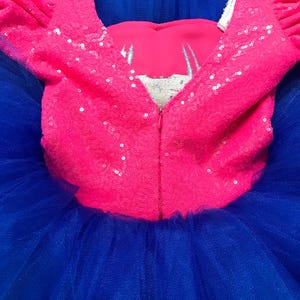 May include: A vibrant pink sequined bodice with short sleeves and a deep V-neckline, paired with a voluminous blue tulle skirt. The bodice features a silver embroidered design and a full-length zipper. This is a children's dress.