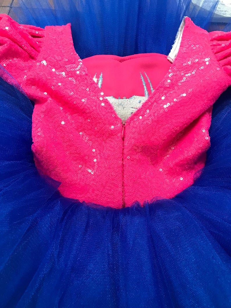 May include: A vibrant pink sequined bodice with short sleeves and a deep V-neckline, paired with a voluminous blue tulle skirt. The bodice features a silver embroidered design and a full-length zipper. This is a children's dress.