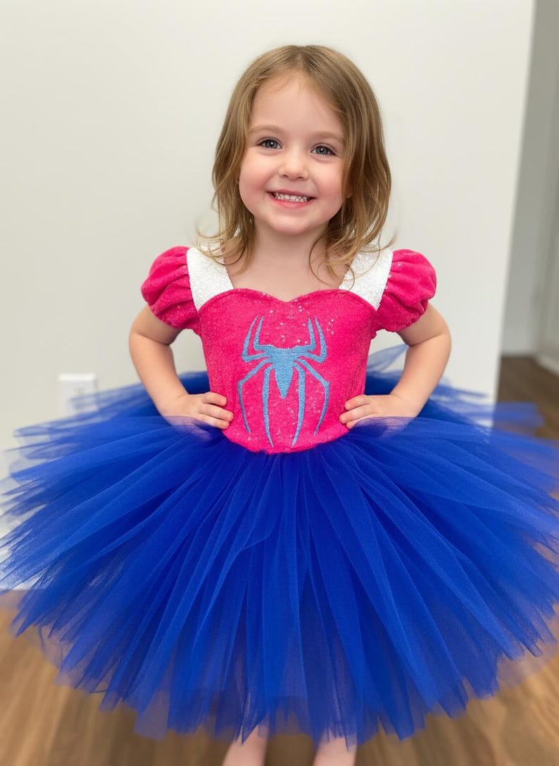 May include: A pink and blue Spider-Man-themed tutu dress. The bodice is pink with a blue spider emblem, white trim, and short sleeves. The skirt is a full, vibrant blue tulle. A child is wearing the dress.