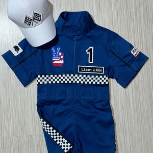 May include: A blue racing jumpsuit with a checkered pattern, a peace sign with an American flag, and the number 1. The jumpsuit has the text "Liam A RH(+) ". A white baseball cap with a checkered flag design is also included.