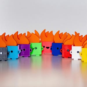 May include: A row of 14 small, colorful, 3D printed figurines with orange flames on top. Each figurine has a different color and a simple, happy face.