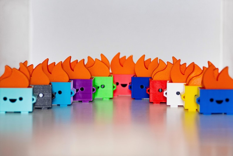 May include: A row of 14 small, colorful, 3D printed figurines with orange flames on top. Each figurine has a different color and a simple, happy face.