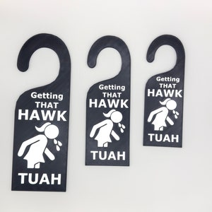 May include: Three black door hangers with a white silhouette of a person throwing up and the text "Getting That Hawk Tuah".
