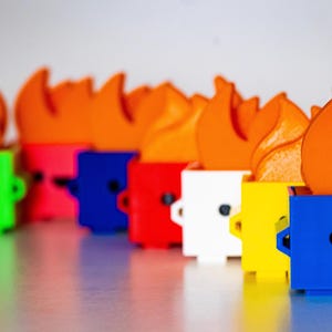 May include: A row of colorful toy trash cans with orange flames on top. Each trash can has a different color and a cute cartoon face.