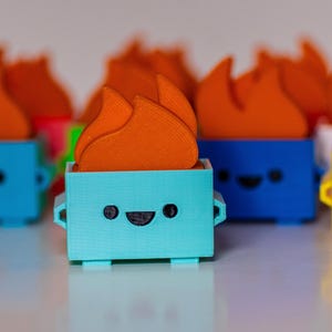May include: A collection of small, colorful, 3D printed figurines with a flame design on top. Each figurine has a happy face and is made of a different color plastic: blue, yellow, and turquoise.