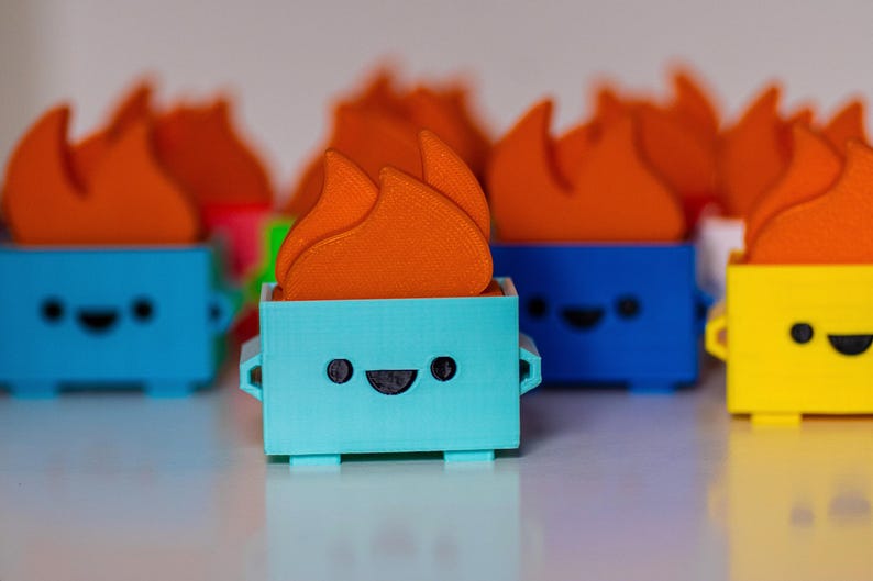 May include: A collection of small, colorful, 3D printed figurines with a flame design on top. Each figurine has a happy face and is made of a different color plastic: blue, yellow, and turquoise.