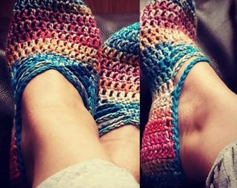 May include: A pair of colorful crocheted slippers with a striped pattern in shades of blue, pink, and yellow. The slippers are made with a chunky yarn and have a simple, comfortable design.