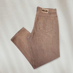 Pode incluir: Um par de calças de ganga castanhas com um design clássico de cinco bolsos. As calças de ganga apresentam um aspeto desbotado e uma aplicação de couro na cintura traseira. As calças de ganga Levi's são um básico de roupa casual.