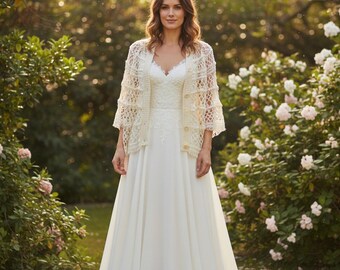Pode incluir: Um vestido branco longo até ao chão com decote em V e detalhes em renda no corpete, combinado com um casaco de malha de croché cor de creme aberto à frente com três botões e mangas três quartos usado sobre o vestido.
