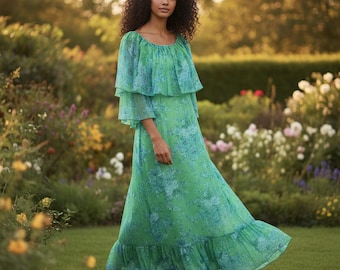May include: A flowing, floor-length green dress with a floral pattern in shades of blue. The dress features a ruffled neckline and sleeves, and a tiered skirt. The model is standing in a garden setting with flowers in the background.
