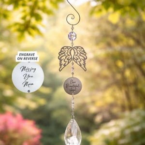 May include: A memorial wind chime with a decorative design. The chime features a metal S-shaped hook, a purple crystal, angel wings, and a round pendant with the text "Our Beautiful Angel". A clear crystal teardrop hangs at the bottom.