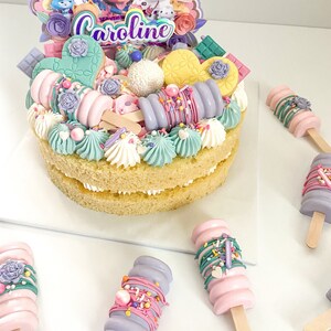 Peut inclure: Un g&acirc;teau &agrave; deux &eacute;tages d&eacute;cor&eacute; de gla&ccedil;age pastel, de p&eacute;pites et de bonbons. Le g&acirc;teau est surmont&eacute; d'une pancarte qui dit "Caroline".
