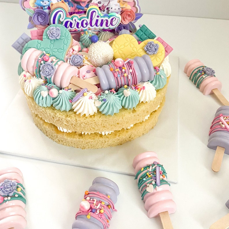 Peut inclure: Un g&acirc;teau &agrave; deux &eacute;tages d&eacute;cor&eacute; de gla&ccedil;age pastel, de p&eacute;pites et de bonbons. Le g&acirc;teau est surmont&eacute; d'une pancarte qui dit "Caroline".