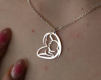 May include: A silver necklace with a heart-shaped pendant featuring a cutout design of a mother and child.