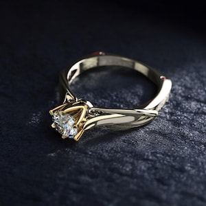 Può includere: Un anello di fidanzamento in oro e argento con un grande diamante trasparente. L'anello presenta un design a fascia attorcigliata unico e un'incastonatura in oro che tiene il diamante. L'anello è presentato su una superficie scura e strutturata.