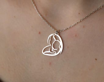 May include: A silver necklace with a heart-shaped pendant featuring a cutout design of a mother holding a baby.