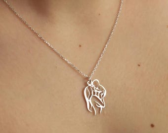 May include: A silver necklace with a pendant featuring a cutout design of two figures embracing. The pendant is a simple, elegant design.