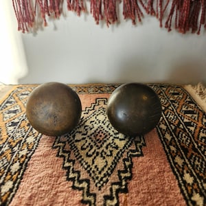 May include: Two dark brown wooden spheres on a pink and brown patterned rug.