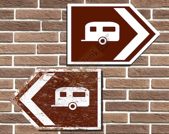 Op de afbeelding: Twee bruine en witte richtingborden met witte pijlen die in tegengestelde richtingen wijzen. Elk bord heeft een wit silhouet van een caravan.
