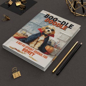 May include: A hardcover journal titled "Boo-Doodle" with a cartoon dog in a vampire costume. The journal cover features a dog wearing sunglasses and a cape, with a pumpkin and the text "A Not-So-Spooky Journal for Honey."